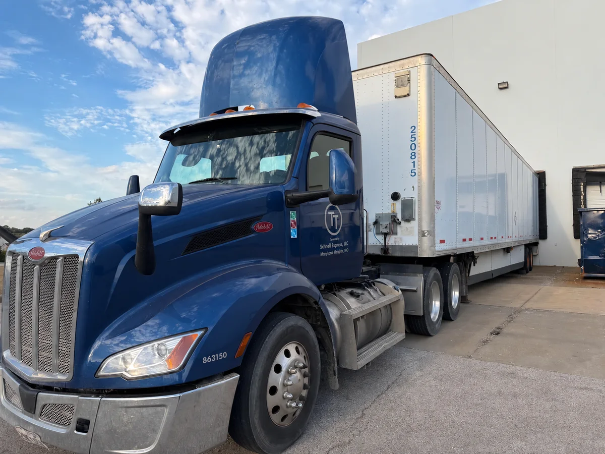 A branded blue Peterbilt tractor and white trailer at a warehouse loading dock