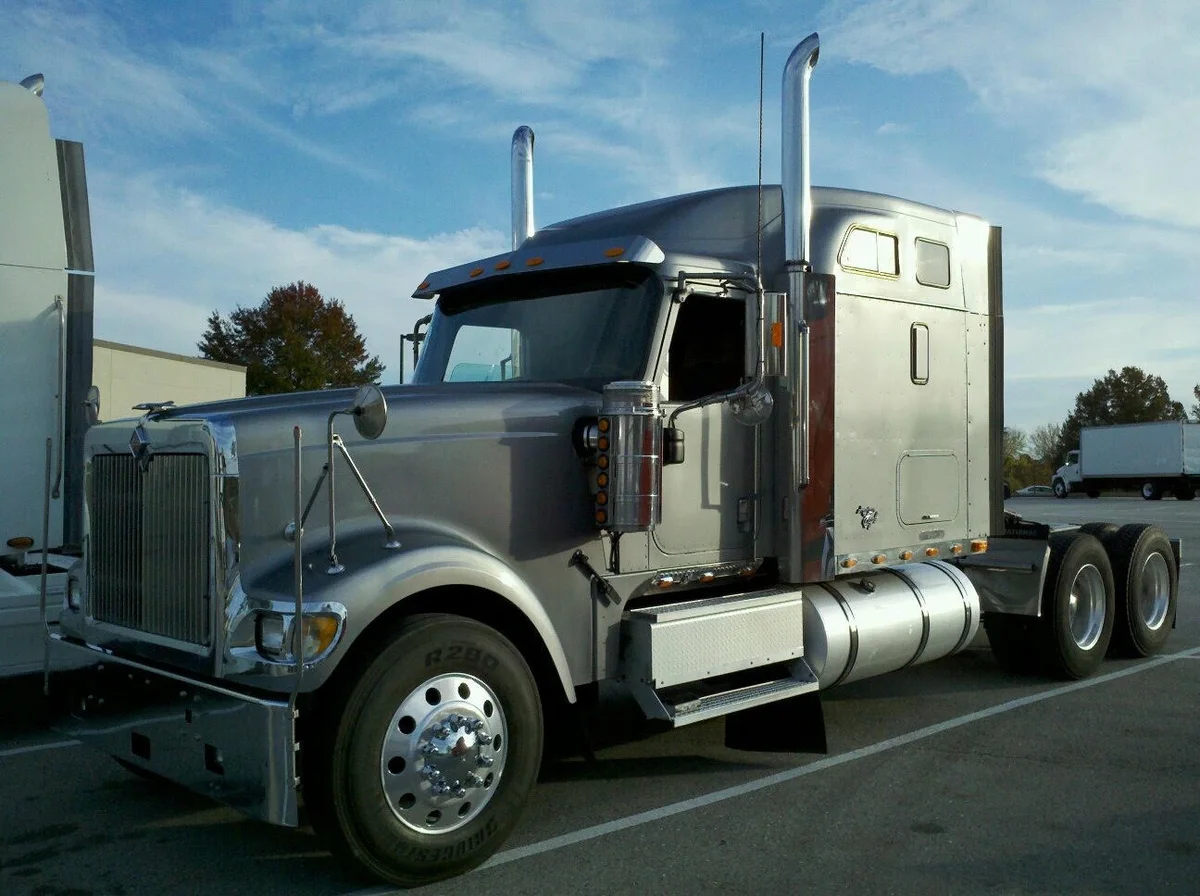 A silver long-nose sleeper tractor parked in a freight yard